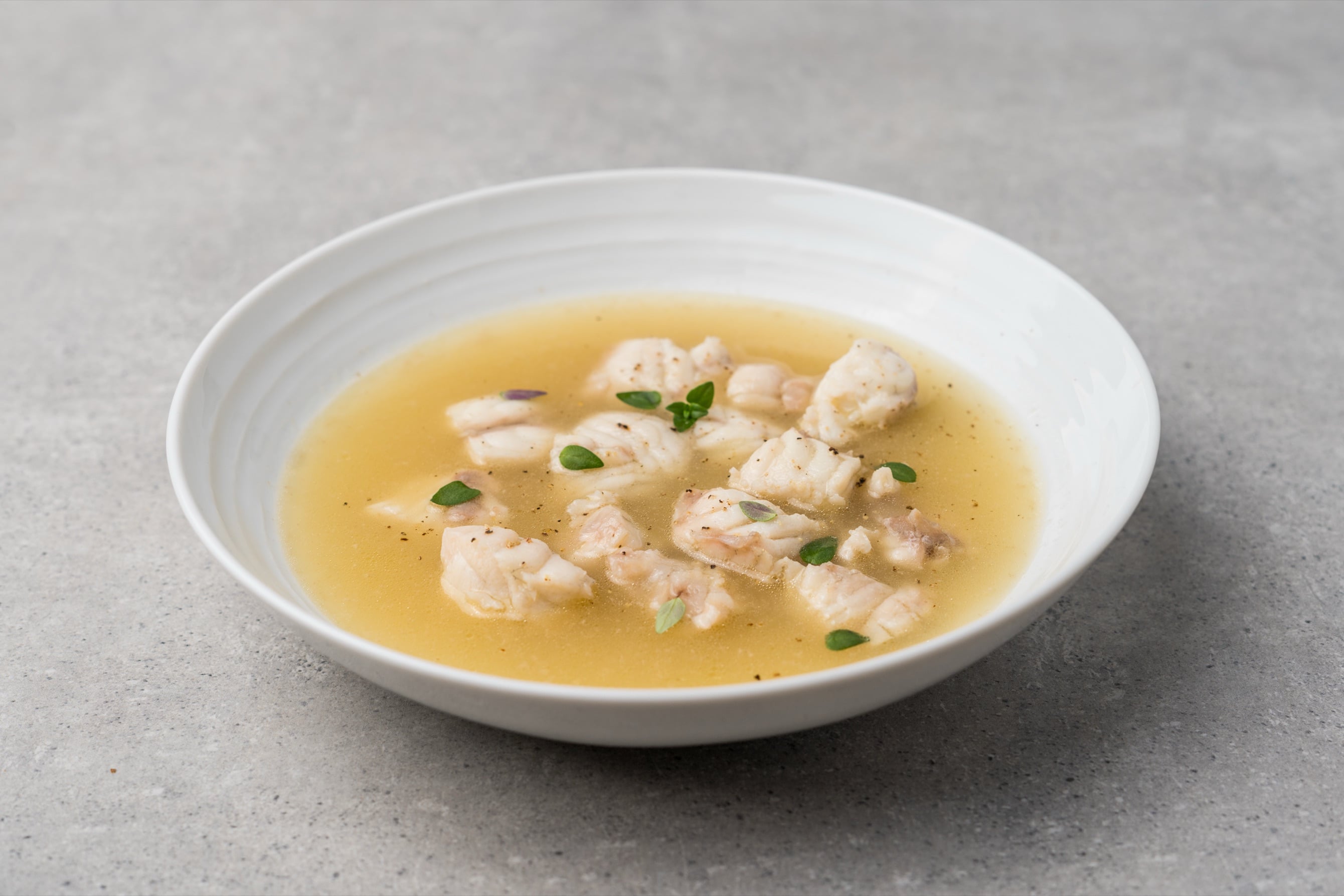 Clear grouper stock with tender fish pieces and fresh herbs in a white bowl